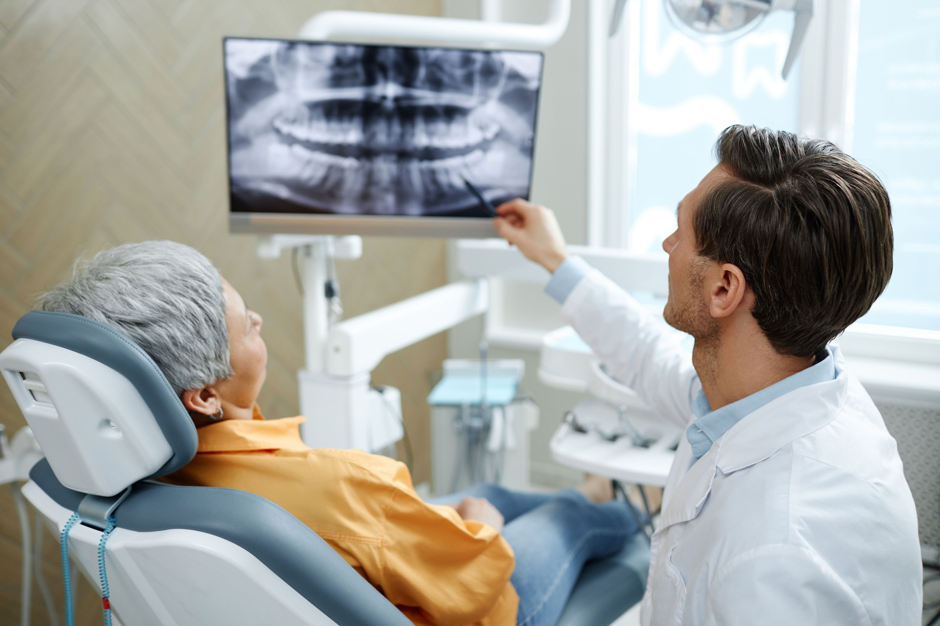 Vista trasera de un dentista masculino señalando la imagen de rayos X del diente en la pantalla